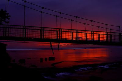 Silhouette bridge over river against romantic sky at sunset