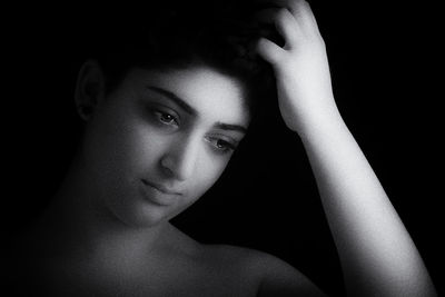 Close-up portrait of shirtless young woman against black background