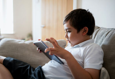 Boy using digital tablet while sitting on sofa at home