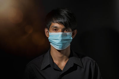 Close-up portrait of man wearing mask against black background