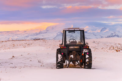 Built structure on field by snowcapped mountain against sky during sunset