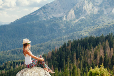 Side view of woman sitting on rock against mountain