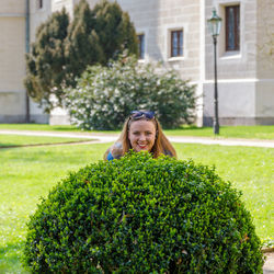 A young beautiful girl looks out from behind a spherical bush.