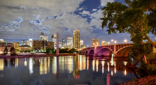 Bridge over river by buildings in city against sky