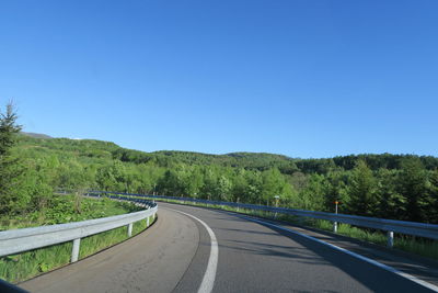 Road leading towards mountains against clear blue sky