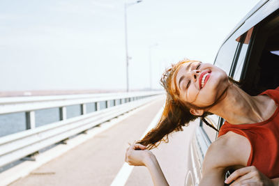 Woman smiling while sitting on railing against sky