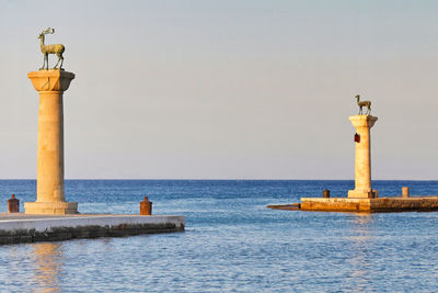 Lighthouse by sea against clear sky