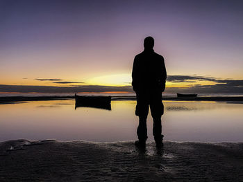 Rear view of silhouette man standing on beach against sky during sunset