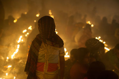 Man covering face with fabric while standing by crowd at night