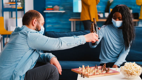 Couple wearing mask toasting beer while playing chess