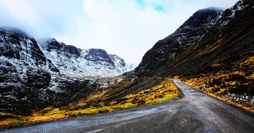 Road by mountains against sky during winter