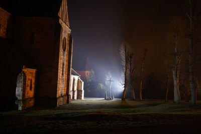 Bare trees on field by church at illuminated night