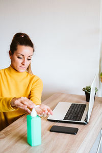 Young woman using hand sanitizer while sitting on table