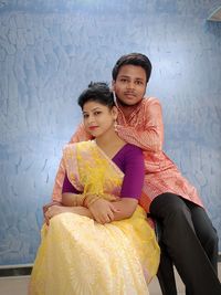 Portrait of young couple sitting against wall at home