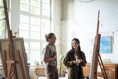 Happy women discussing over painting on easel in art studio