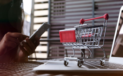 Midsection of woman using laptop by shopping cart while sitting on table