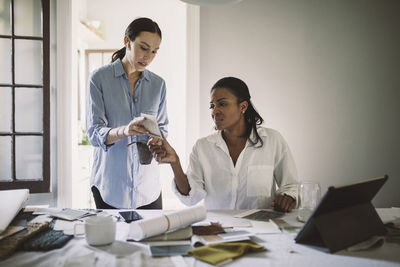 Female designers discussing about fabric swatch while working at table in home office