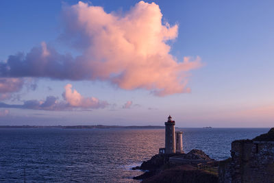 Lighthouse by sea against sky during sunset