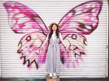 Portrait of woman standing against pink butterfly wings graffiti on closed shutter