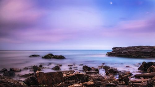 View of rocks on coast of sea against cloudy sky