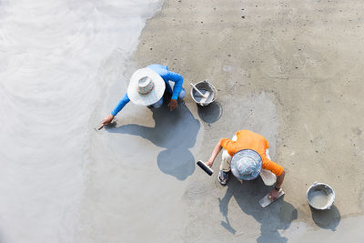 Directly above shot of workers leveling cement on footpath