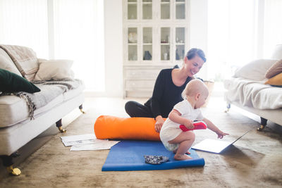 Smiling mother looking at daughter pointing at laptop while practicing yoga in living room