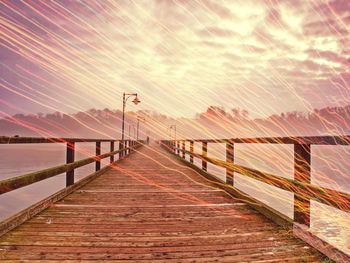 Footbridge over sea against sky during sunset