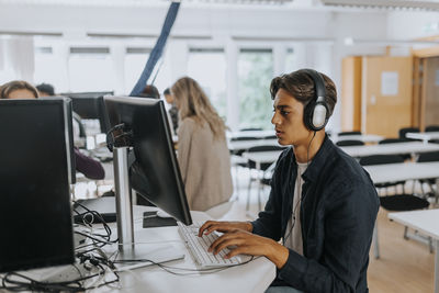 Teenage boy listening through headphones while using computer in school lab