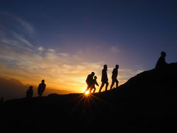 Silhouette people standing on land against sky during sunset