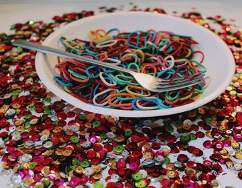 Close-up of multi colored rubber bands and sequins in bowl on table