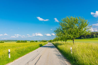 Empty road amidst field against blue sky