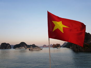 Scenic view of flag by sea against clear blue sky