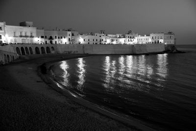 Illuminated buildings by sea against clear sky at night