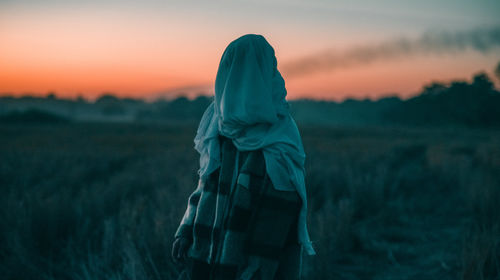 Rear view of woman standing against sky during sunset