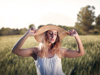 Portrait of young woman standing on field against sky