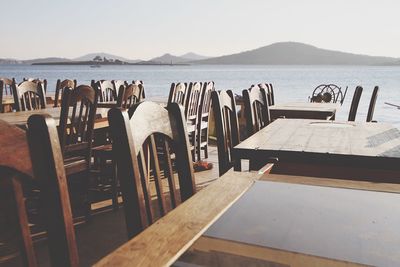 Empty chairs and tables by river against clear sky