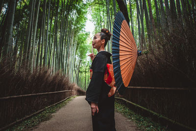 Side view of woman with umbrella standing amidst trees