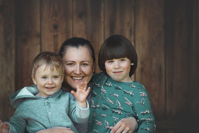 Portrait of smiling mother with kids against wooden wall