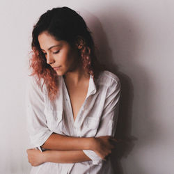 Young woman looking down while standing against white background