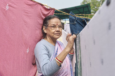 Portrait of a simple looking mature indian woman hanging freshly washed laundry to dry in the sun