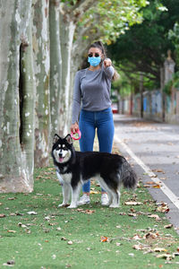 Full length of woman wearing mask with dog standing in forest