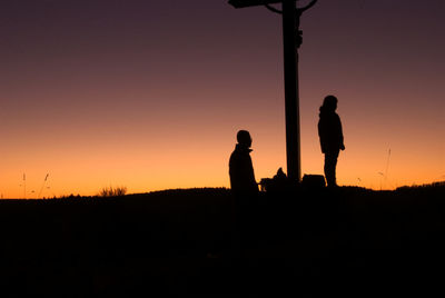 Silhouette men standing on field against orange sky