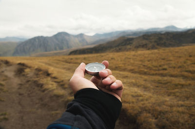 First-person view of a male traveler s hand holding a magnetic compass against the backdrop