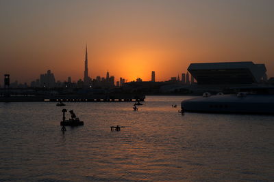Silhouette of buildings by river during sunset