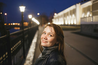 Portrait of smiling young woman on illuminated bridge at night