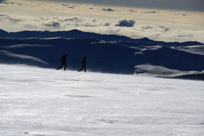 Silhouette people on snowcapped mountains against sky