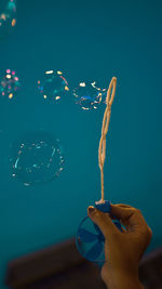 Close-up of hand blowing bubbles  against blue background