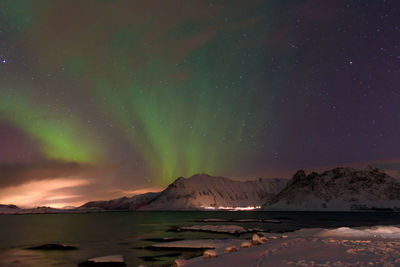 Scenic view of lake by snowcapped mountains against sky at night