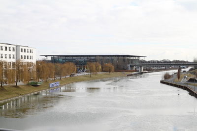 Frozen river in city against sky during winter