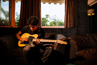 Man playing guitar on sofa at home